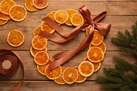 Decorative wreath made with dry oranges, ribbon and fir branches on wooden table, flat layの写真素材