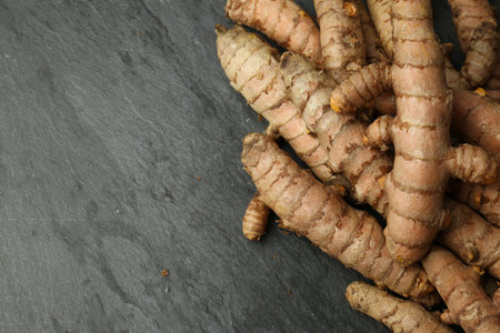 Many raw turmeric roots on black textured table, flat lay. Space for text