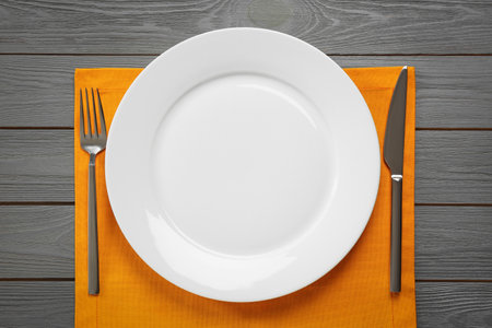 Clean plate and shiny silver cutlery on gray wooden table, flat lay