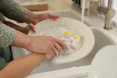Mother and daughter washing plate above sink, closeupの写真素材