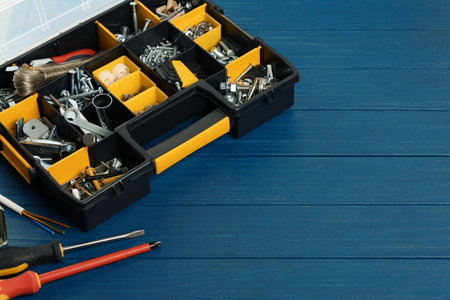 Plastic box with different furniture fittings and tools on blue wooden table, space for text