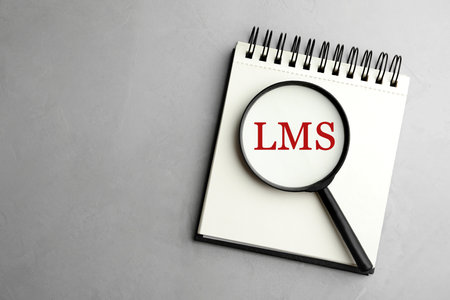 Learning Management System. Notebook with abbreviation LMS and magnifying glass on light background, top viewの写真素材