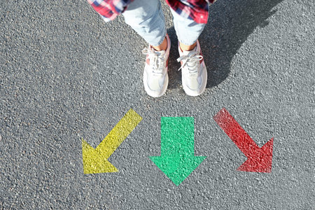 Choice of way. Woman standing in front of drawn marks on the road, closeup. Colorful arrows pointing in different directionsの写真素材