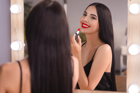 Young woman applying beautiful red lipstick in front of mirror indoorsの写真素材