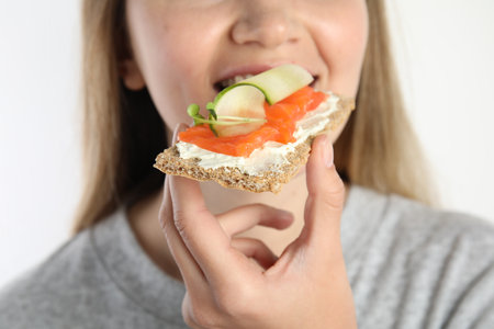 Woman eating fresh rye crispbread with cream cheese, salmon and cucumber on white background, closeupの写真素材