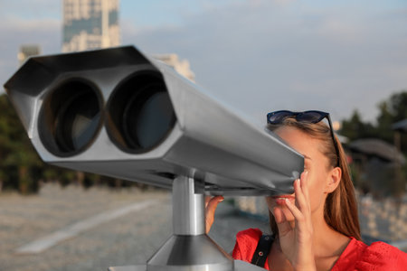 Young woman looking through tourist viewing machine at observation deckの写真素材