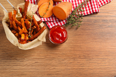 Sweet potato fries, thyme and ketchup on wooden table, flat lay. Space for text