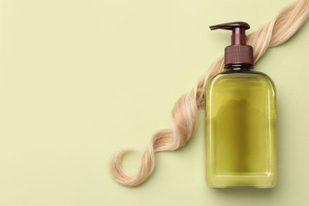 Lock of hair and shampoo bottle on olive background, flat lay. Space for textの写真素材