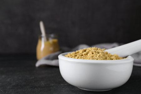 Mortar with mustard powder on black table. Space for textの写真素材