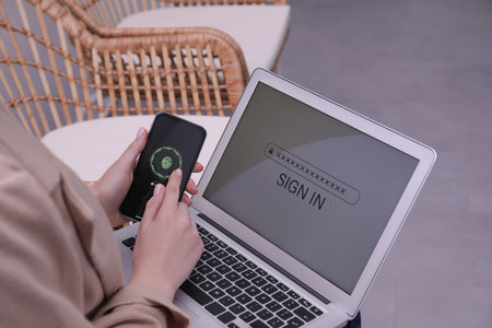Woman unlocking smartphone with fingerprint scanner, closeup. Her laptop password protected toの写真素材