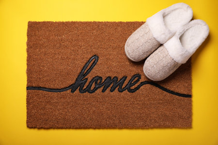 Doormat with word Home and slippers on yellow background, flat layの写真素材