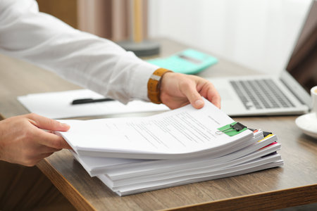 Man working with documents at wooden table in office, closeup