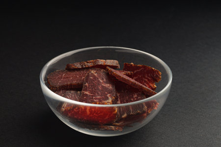 Bowl with pieces of delicious beef jerky on black tableの写真素材