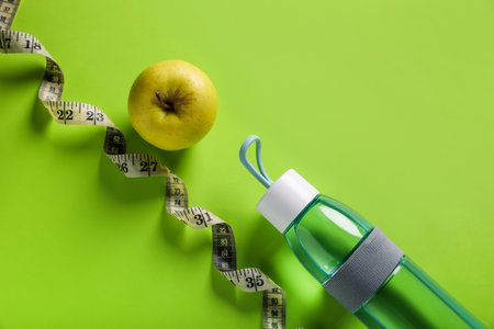 Measuring tape, bottle with water and apple on light green background, flat lay. weight control conceptの写真素材