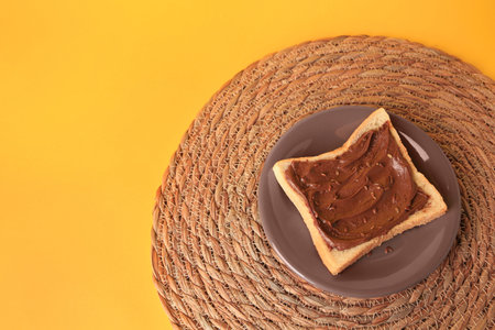 Tasty toast with chocolate paste and flax seeds on yellow background, above view. Space for text