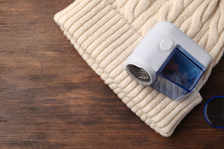 Modern fabric shaver and white knitted hat on wooden table, top view. Space for textの写真素材