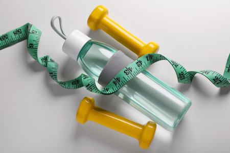 Measuring tape, dumbbells and bottle with water on white background, above view. weight control...