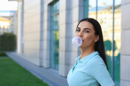 Beautiful woman blowing gum near building outdoors, space for textの写真素材