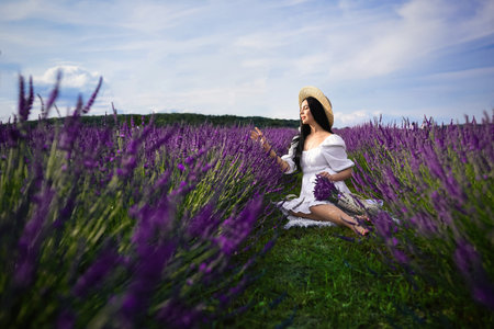 Beautiful young woman sitting in lavender fieldの写真素材