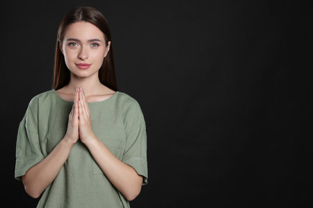 Woman with clasped hands praying on black background, space for textの写真素材