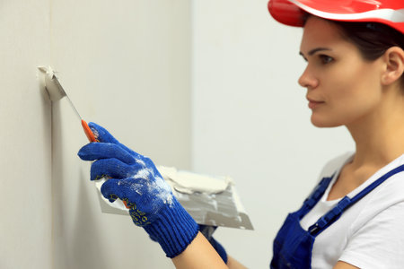 Professional worker in hard hat plastering wall with putty knives, focus on handの写真素材