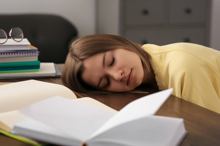 Young tired woman sleeping near books at wooden table indoorsの写真素材