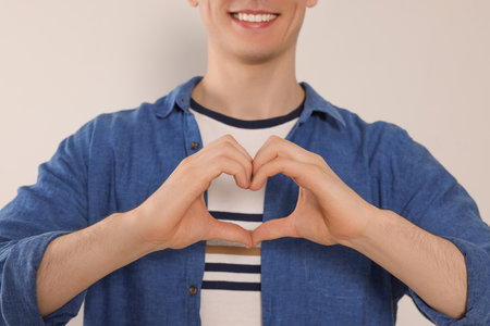 Happy volunteer making heart with his hands on light background, closeupの写真素材