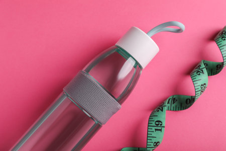Measuring tape and bottle of water on pink background, flat lay. weight control conceptの写真素材