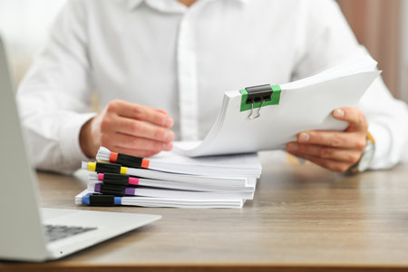 Man working with documents at wooden table in office, closeup