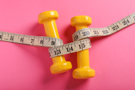 Measuring tape and dumbbells on pink background, flat lay. weight control conceptの写真素材