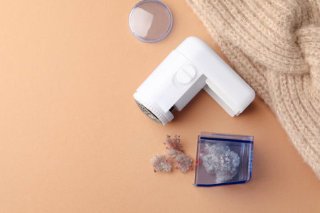 Modern fabric shaver with fuzz and knitted headdress on pale orange background, flat lay. Space for textの写真素材