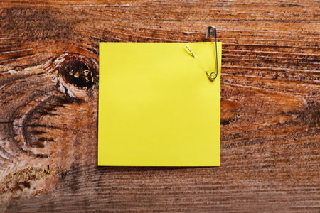 Yellow paper note attached with safety pin on wooden table, top view. Space for text
