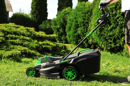 Man cutting grass with lawn mower in garden on sunny day, closeup