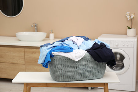 Plastic laundry basket overfilled with clothes on white table in bathroomの写真素材