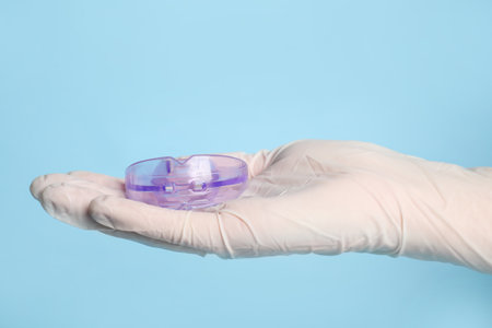 Dentist holding mouth guard on light blue background, closeup. Bit correctionの写真素材