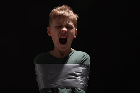 Scarred little boy tied up and taken hostage on dark background. Space for textの写真素材