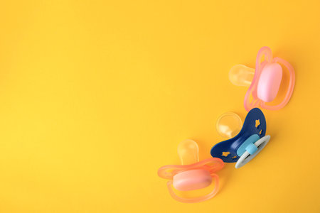 Colorful baby pacifiers on orange background, flat lay. Space for textの写真素材
