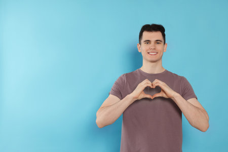 Happy volunteer making heart with his hands on light blue background. Space for textの写真素材