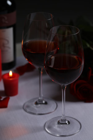 Glasses of red wine, rose flowers and burning candle on white table. romantic atmosphereの写真素材
