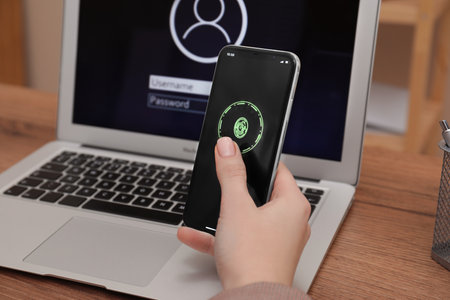 Woman holding blocked smartphone with fingerprint identification near laptop at workplace , closeup....