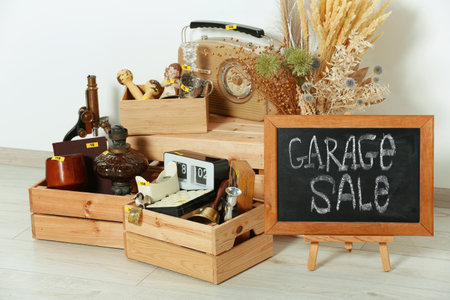 Sign Garage Sale written on blackboard and many different stuff near white wall