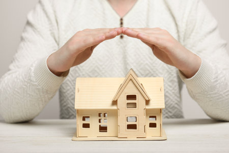 home security concept. Man covering house model on white wooden table, closeupの写真素材