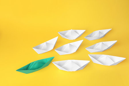 Group of paper boats following green one on yellow background. leadership concept