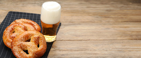 Tasty pretzels and glass of beer on wooden table, space for text. banner design