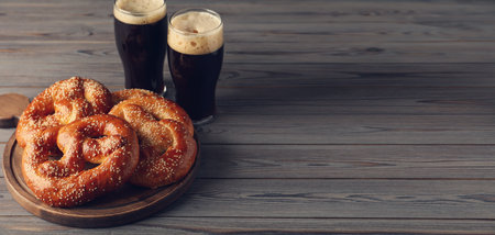 Tasty pretzels and glasses of beer on wooden table, space for text. banner design