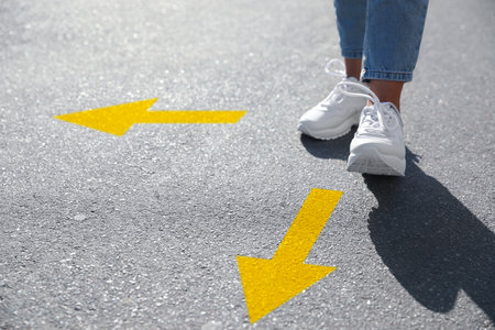 Choice of way. Woman walking to drawn mark on road, closeup. yellow arrows pointing in different directionsの写真素材