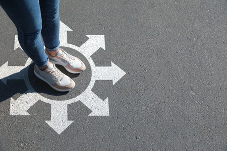 Choice of way. Woman standing in drawn circle with marks on the road, closeup. White arrows pointing in different directionsの写真素材