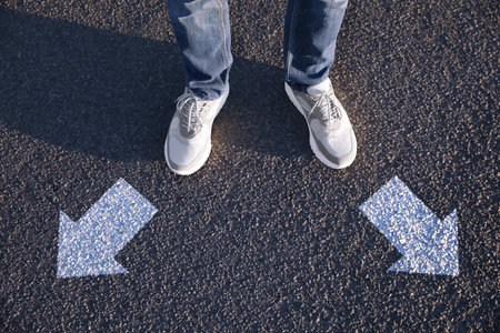 Choice of way. Man standing in front of drawn marks on the road, closeup. White arrows pointing in...
