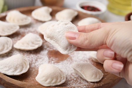 Woman holding raw dumpling (varenyk) with tasty filling on wooden board, closeup