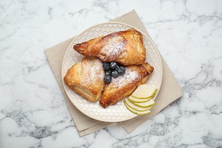 Fresh tasty puff pastry with sugar powder, pear and blueberries served on white marble table, top viewの写真素材